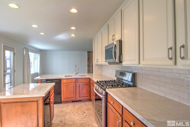 kitchen featuring light countertops, appliances with stainless steel finishes, brown cabinetry, a sink, and a kitchen island