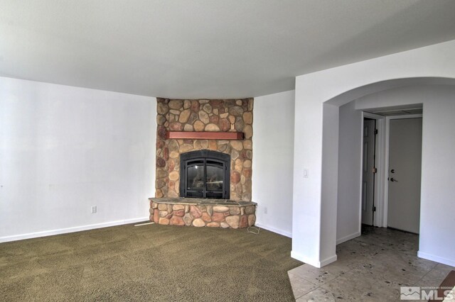 unfurnished living room with a stone fireplace, carpet, and baseboards