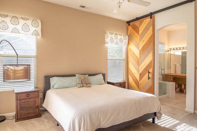 bedroom featuring light carpet, a barn door, visible vents, baseboards, and ensuite bath