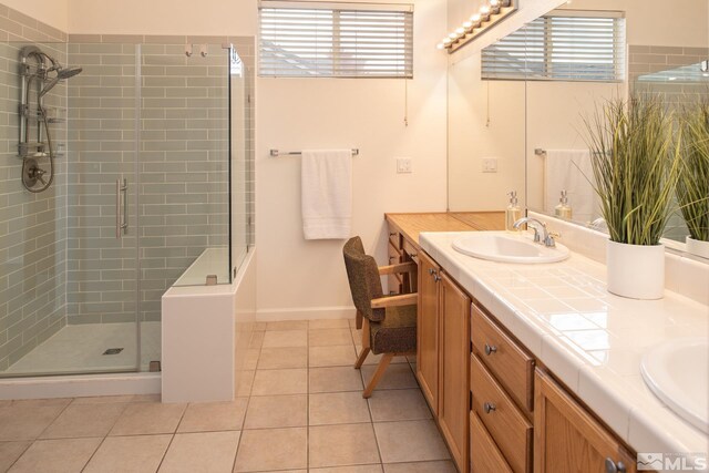 full bath featuring a sink, baseboards, tile patterned floors, double vanity, and a stall shower