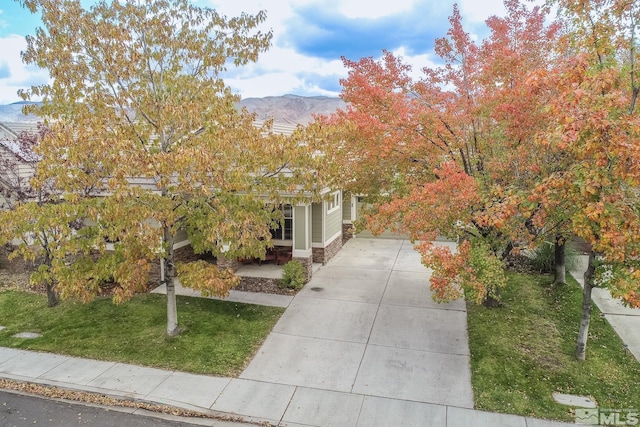 obstructed view of property with stone siding, a mountain view, and a front lawn