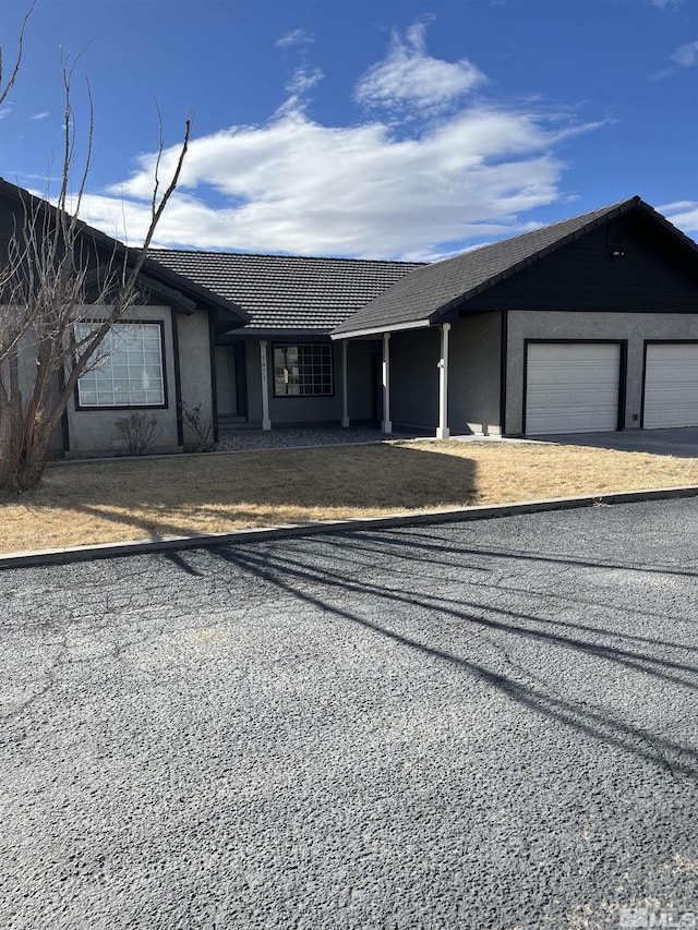 ranch-style home featuring a garage, driveway, a tiled roof, and stucco siding