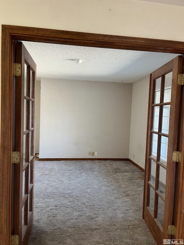 carpeted spare room featuring french doors, a textured ceiling, and baseboards