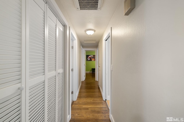 hall featuring visible vents, dark wood-style flooring, attic access, and baseboards