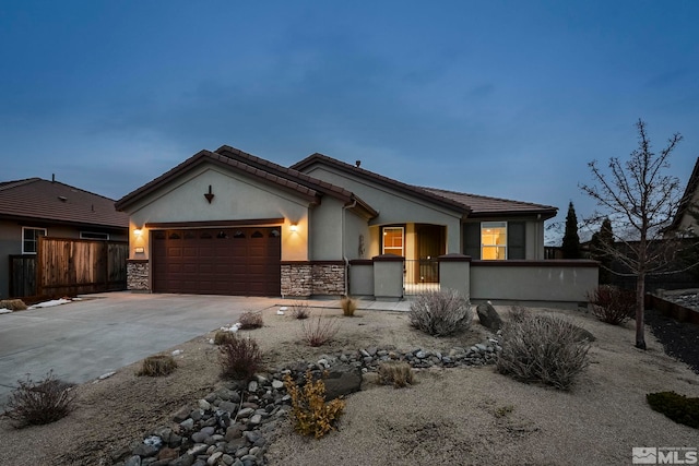 view of front of home featuring concrete driveway, stone siding, an attached garage, fence, and stucco siding