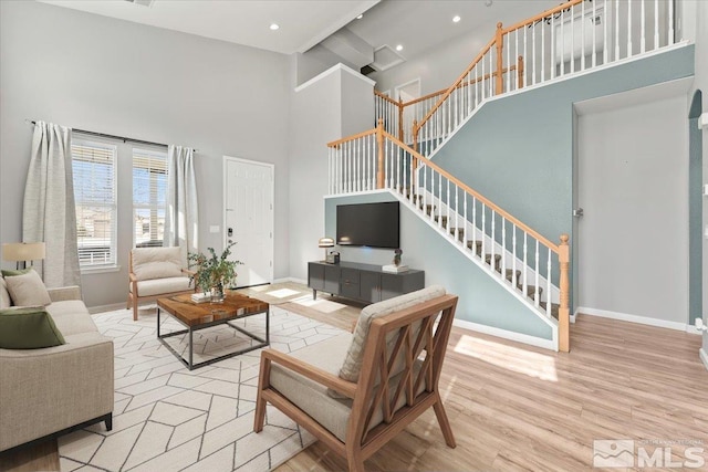 living area with a high ceiling, baseboards, stairway, and light wood finished floors