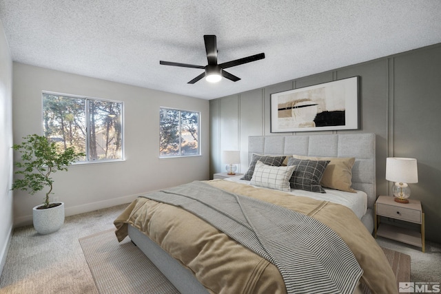 bedroom featuring light colored carpet, a decorative wall, a ceiling fan, a textured ceiling, and baseboards