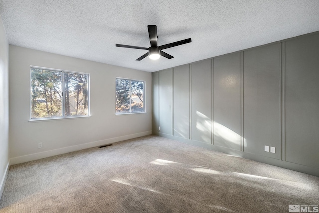 empty room featuring light carpet, a textured ceiling, visible vents, and baseboards