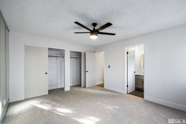 unfurnished bedroom featuring two closets, carpet flooring, connected bathroom, a textured ceiling, and baseboards