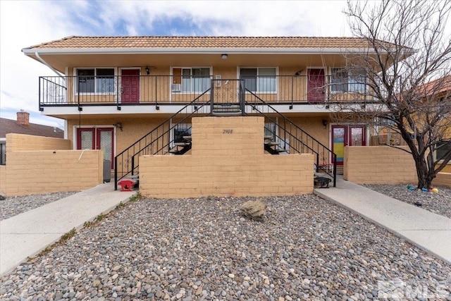 view of front facade featuring fence, stairway, and stucco siding