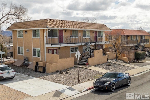 multi unit property featuring a tiled roof, stairway, and stucco siding