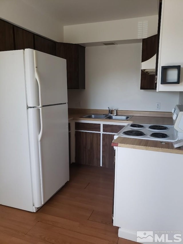 kitchen featuring white appliances, light wood finished floors, light countertops, dark brown cabinets, and a sink