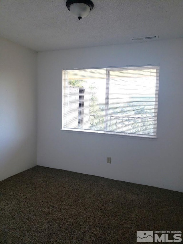 carpeted spare room featuring a textured ceiling and visible vents