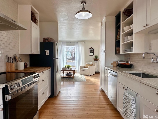 kitchen with light stone counters, under cabinet range hood, a sink, white cabinetry, and appliances with stainless steel finishes