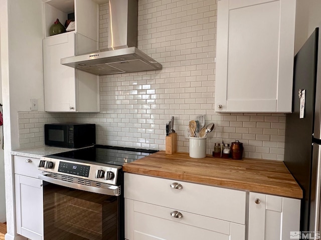 kitchen with decorative backsplash, appliances with stainless steel finishes, white cabinetry, wall chimney range hood, and butcher block countertops