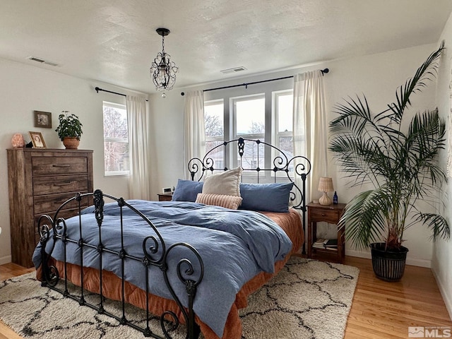 bedroom with baseboards, a textured ceiling, visible vents, and light wood-style floors