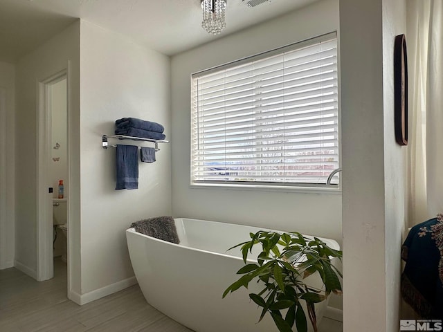 full bathroom with a soaking tub, a healthy amount of sunlight, baseboards, and toilet