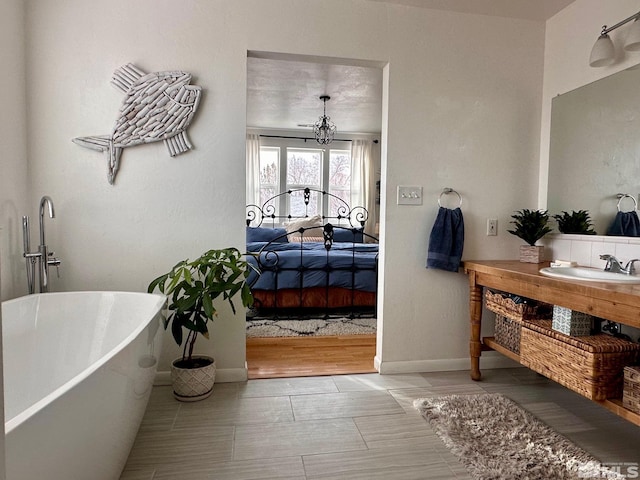 ensuite bathroom with baseboards, a soaking tub, ensuite bath, vanity, and a notable chandelier