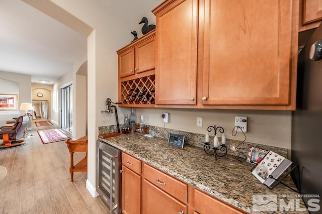 kitchen with light stone counters, wine cooler, brown cabinets, and light wood-style flooring