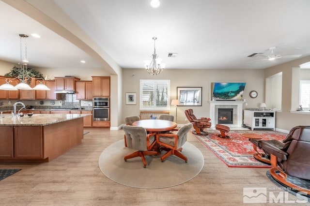 kitchen with decorative light fixtures, a tiled fireplace, brown cabinetry, open floor plan, and light stone countertops