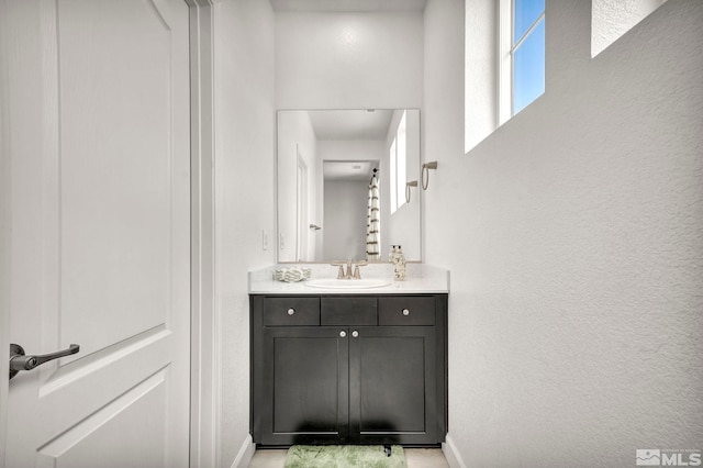 bathroom with a textured wall, baseboards, and vanity