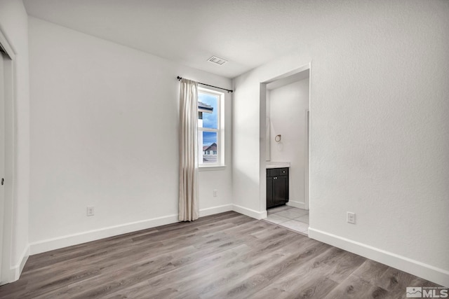 unfurnished bedroom featuring light wood-style flooring, ensuite bath, visible vents, and baseboards