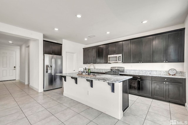 kitchen featuring light stone counters, a kitchen breakfast bar, a kitchen island with sink, stainless steel appliances, and a sink