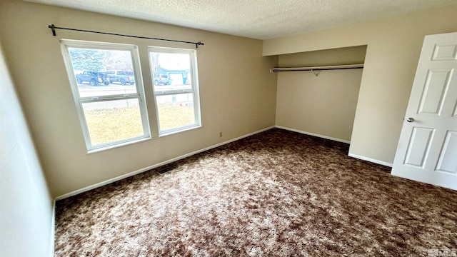 unfurnished bedroom with a textured ceiling, dark colored carpet, a closet, and baseboards