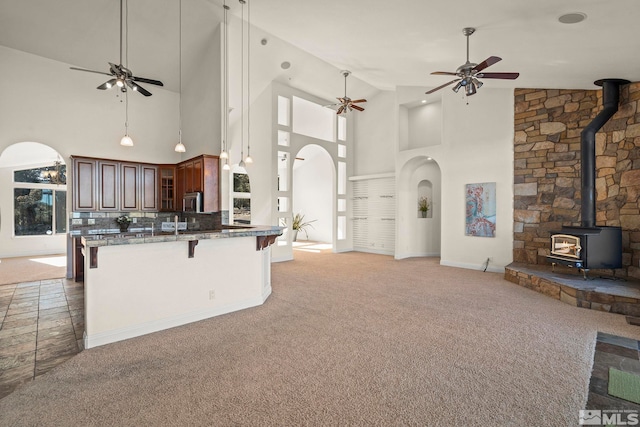 kitchen with glass insert cabinets, a peninsula, open floor plan, a kitchen bar, and a wood stove