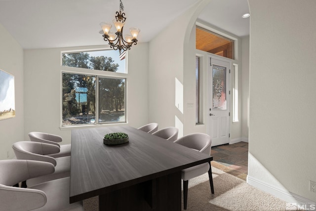 dining area with baseboards, arched walkways, a notable chandelier, and stone finish flooring