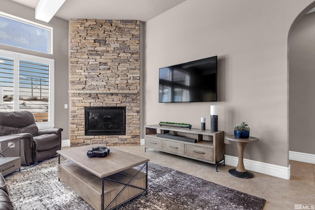 living area featuring baseboards, arched walkways, beamed ceiling, a fireplace, and light tile patterned flooring