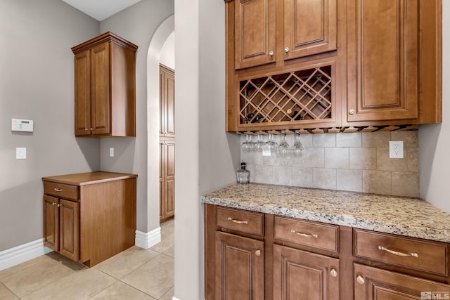 kitchen with light stone counters, brown cabinets, light tile patterned floors, decorative backsplash, and baseboards