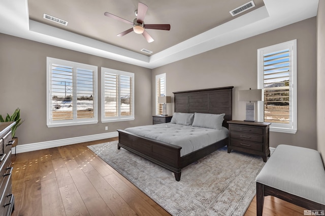 bedroom with a tray ceiling, light wood-style floors, visible vents, and baseboards