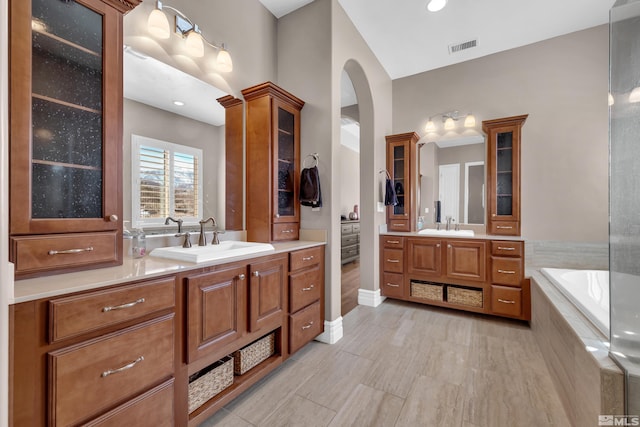 bathroom featuring a relaxing tiled tub, visible vents, and vanity