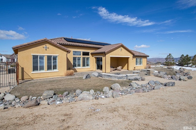 rear view of property featuring a patio, a tile roof, fence, roof mounted solar panels, and stucco siding