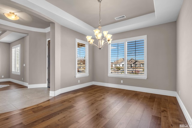 unfurnished dining area featuring a tray ceiling, visible vents, baseboards, and wood finished floors