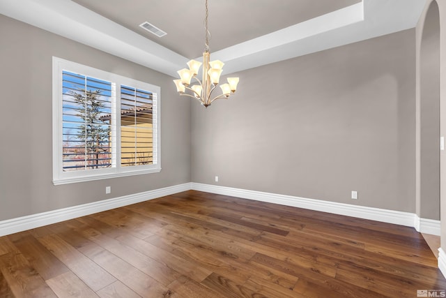 unfurnished room featuring a notable chandelier, dark wood-style flooring, visible vents, baseboards, and a tray ceiling