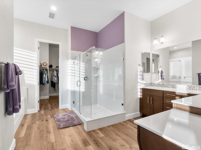 bathroom with visible vents, a spacious closet, a shower stall, vanity, and wood finished floors