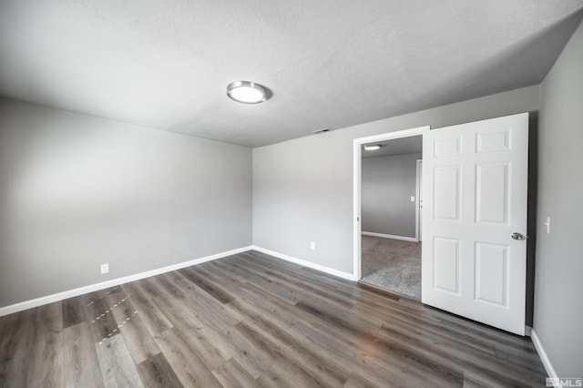 unfurnished bedroom with baseboards, dark wood-style floors, a walk in closet, a textured ceiling, and a closet