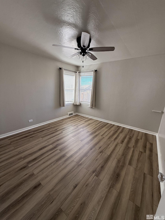 spare room with ceiling fan, visible vents, dark wood finished floors, and baseboards