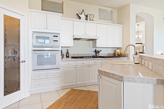 kitchen featuring tile countertops, under cabinet range hood, white appliances, a sink, and white cabinetry