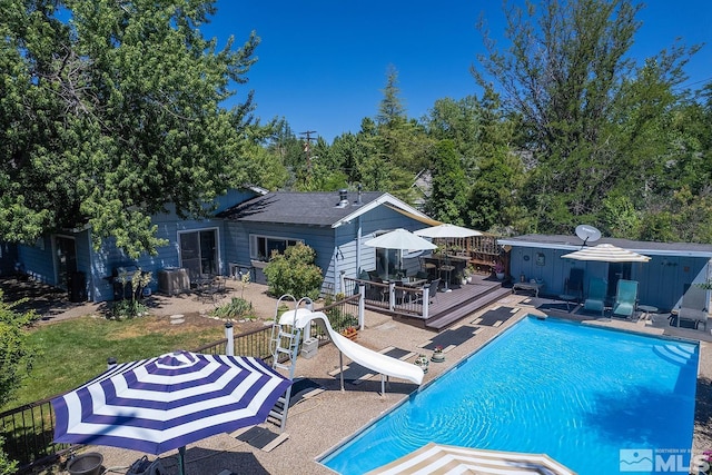 pool featuring a patio area, a deck, a water slide, and an outbuilding