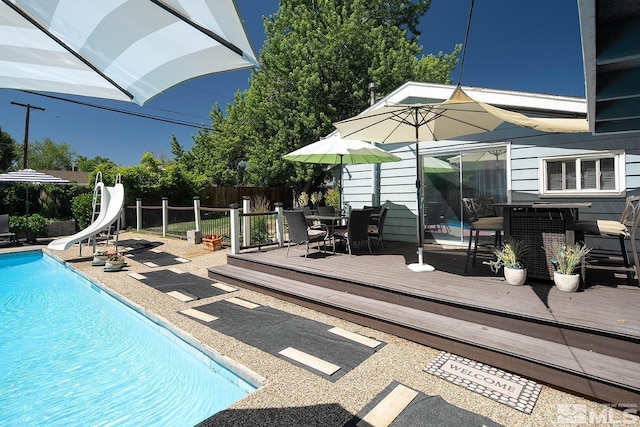 view of swimming pool featuring a water slide, a wooden deck, a fenced in pool, and fence