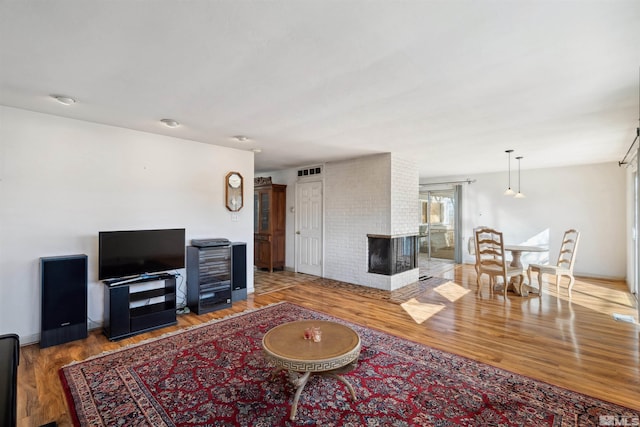 living room with baseboards, visible vents, a multi sided fireplace, and wood finished floors