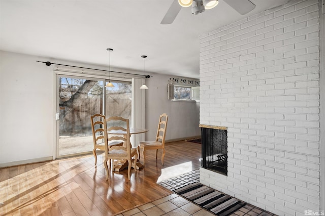 dining space featuring a healthy amount of sunlight, a brick fireplace, a ceiling fan, and wood finished floors