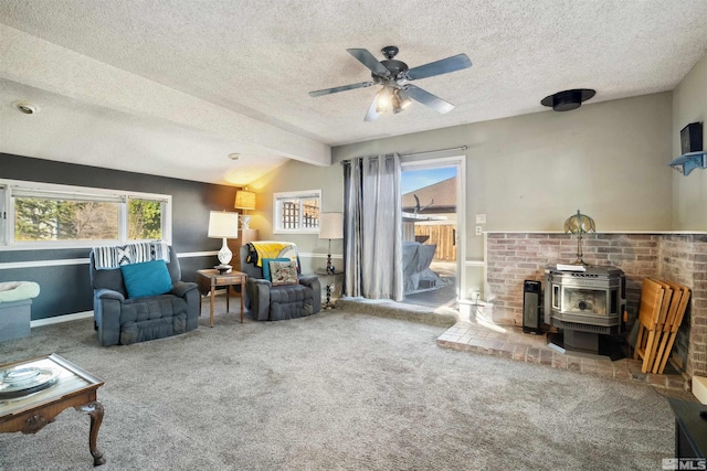 carpeted living area featuring a textured ceiling, lofted ceiling with beams, a wood stove, and a ceiling fan