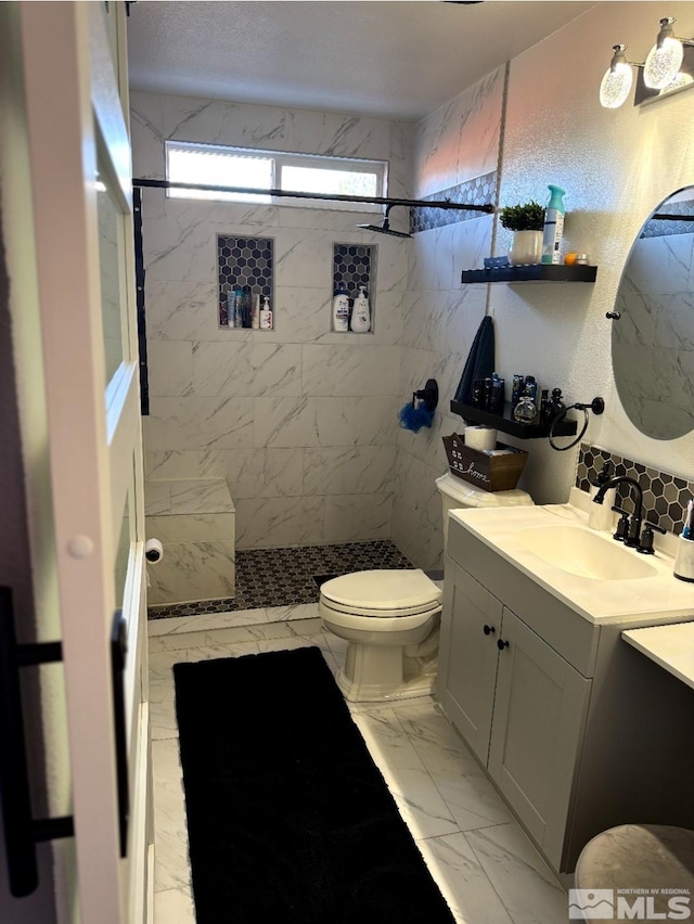 full bathroom with marble finish floor, vanity, a tile shower, and toilet