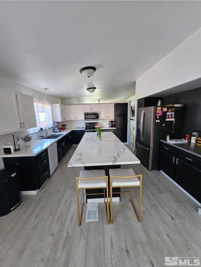 kitchen featuring a center island, stainless steel appliances, tasteful backsplash, a sink, and dark cabinetry