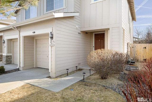 doorway to property featuring board and batten siding, fence, and a garage