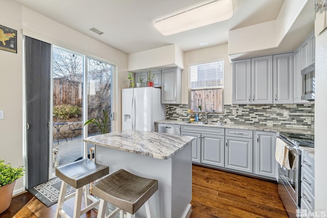 kitchen featuring visible vents, appliances with stainless steel finishes, a kitchen breakfast bar, a center island, and gray cabinetry